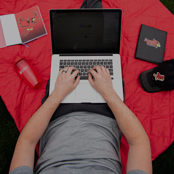 Student using a laptop computer sitting on a red blanket.
