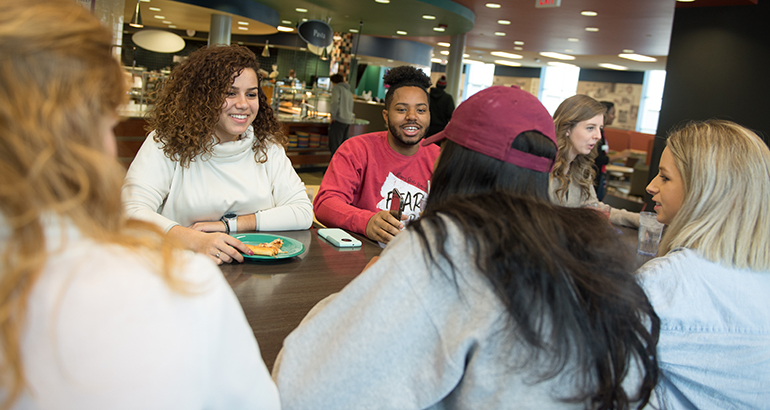Group of students talking and eating at a table in the Watterson dining center.
